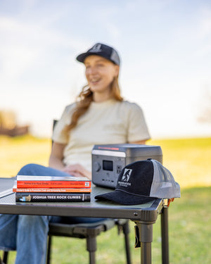 Sasquatch Outdoor Black Hat and 600W Portable Power Station on Camping Table Onsite Lifestyle with Tacy